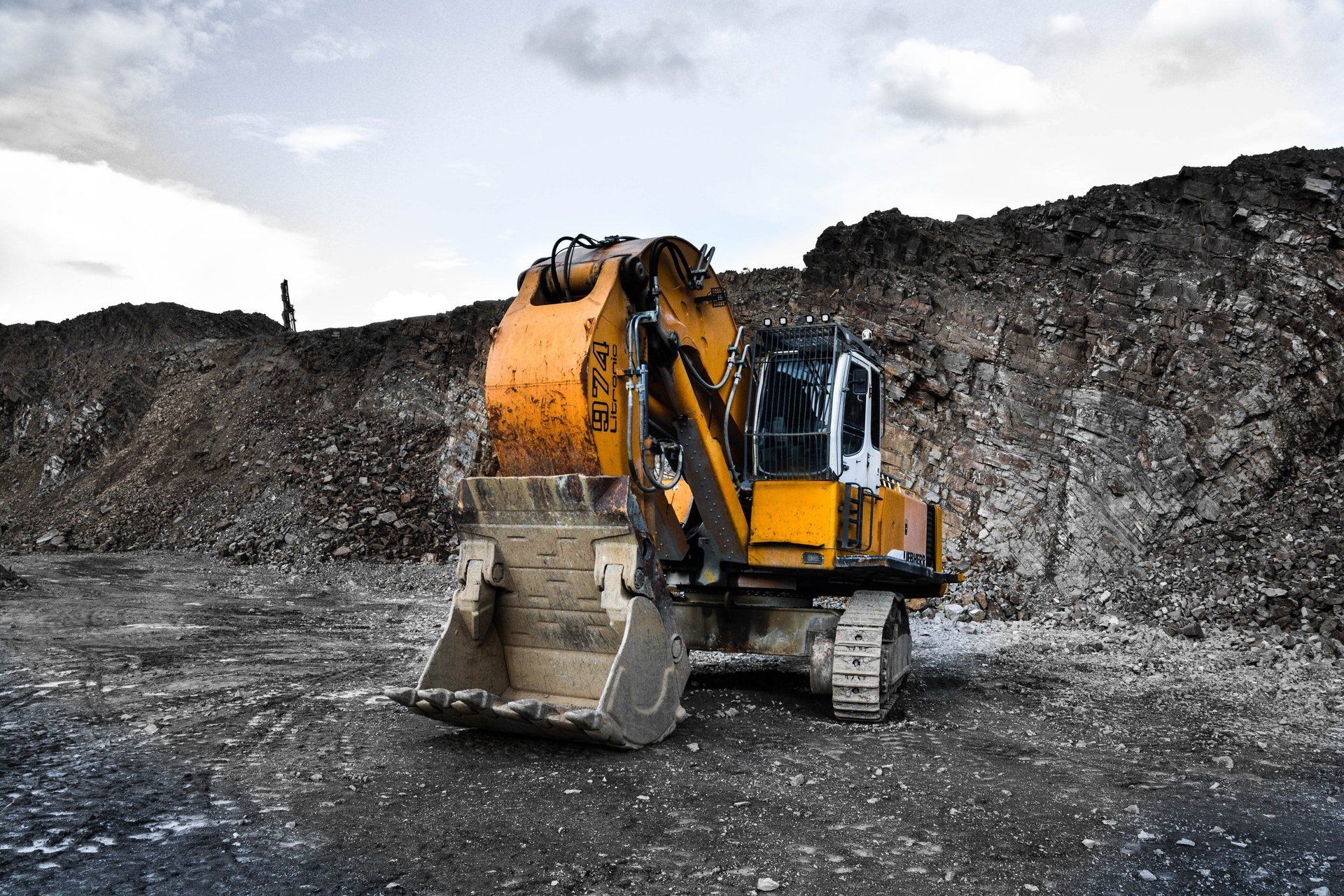 Yellow excavator with a large bucket on a rocky construction site, working near a pile of debris.